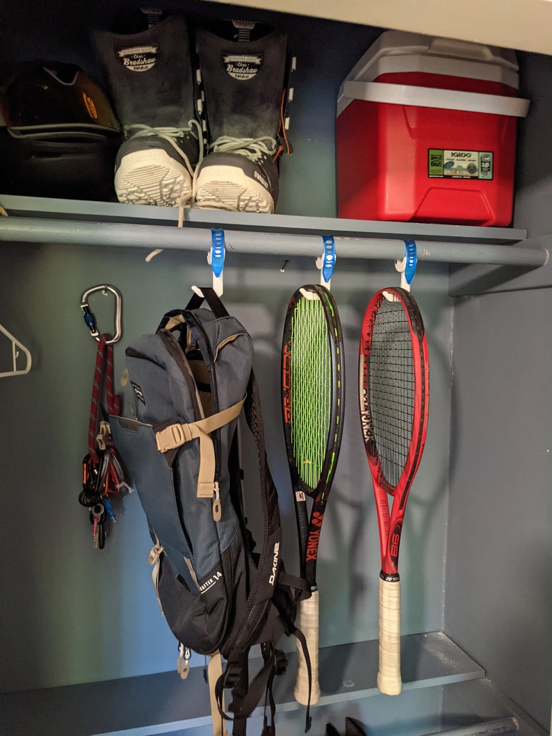 Puede incluir: Un armario blanco con una nevera roja, dos pares de botas de esqu&iacute; blancas y negras, una mochila azul, dos raquetas de tenis y un mosquet&oacute;n con una cuerda colgando de un gancho.