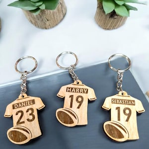May include: Three wooden keychains shaped like rugby jerseys with names and numbers. The keychains are Daniel 23, Harry 19, and Sebastian 19.