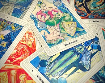 May include: A collection of tarot cards with intricate illustrations. The cards feature images of figures, symbols, and celestial elements in a variety of colors, including blue, red, and yellow. The card labeled "The Empress" is visible.