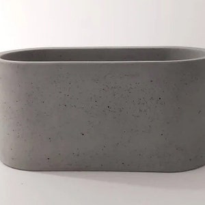 May include: A grey oval concrete planter. The planter has a rough, textured surface.