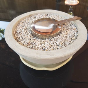 May include: A round concrete fire pit with a metal insert and a layer of small white stones.