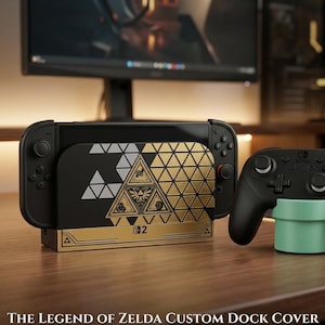 Peut inclure: Un cache-station d'accueil personnalisé noir et doré pour console de jeu vidéo, orné d'un motif géométrique Triforce avec des symboles complexes. Le cache est fixé sur une station d'accueil avec des manettes noires et une manette sans fil.