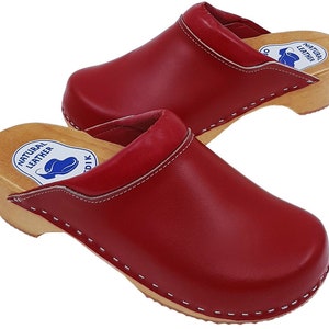 May include: Pair of red leather clogs with wooden soles and white stitching. The clogs have a label that reads "Natural Leather".