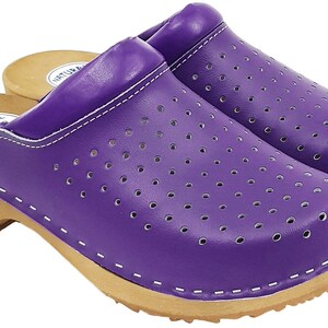 May include: Purple leather clogs with a wooden sole and a perforated design. The clogs have a white stitching detail around the edge of the sole and a label that says "NATURAL LEATHER" on the side.