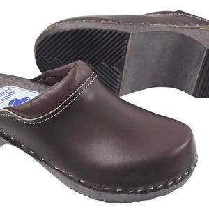 Può includere: Zoccoli in pelle marrone con suola in legno e punta arrotondata. Gli zoccoli hanno un design slip-on con tomaia cucita e suola spessa e scanalata. L'altezza del tacco è di circa 5 cm.