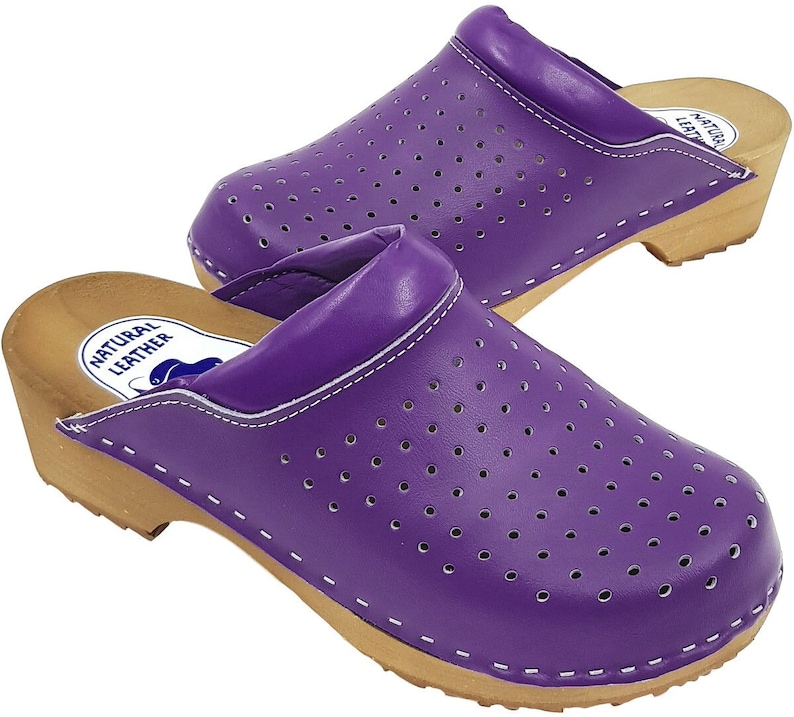 May include: Purple leather clogs with a wooden sole and a perforated design. The clogs have a white stitching detail and a label that reads "Natural Leather".