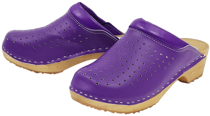 May include: A pair of purple leather clogs with a wooden sole and a perforated design. The clogs have a white stitching detail around the edges.