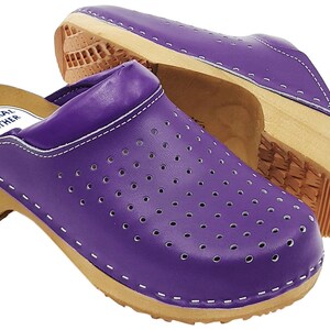 May include: Purple leather clogs with a wooden sole and a white stitch detail. The clogs have a perforated design and the words "Natural Leather" are printed on the inside of the clog.