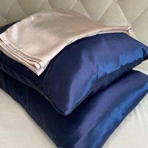 Peut inclure: Deux taies d'oreiller en satin, une bleu marine et une rose pâle, sont empilées l'une sur l'autre. Les taies d'oreiller sont faites d'un matériau doux et soyeux.