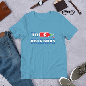 May include: A light blue t-shirt with a red and green hot sauce bottle graphic and the text "YO BALEADAS" in blue and white letters.