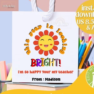 Könnte beinhalten: Weiße Geschenktüte mit einem fröhlichen Sonnengrafik und dem Text "This year is looking BRIGHT!". Enthält den Text "I'm so happy your my teacher" und "From: Madison". Die Tüte ist ein A4-Format.