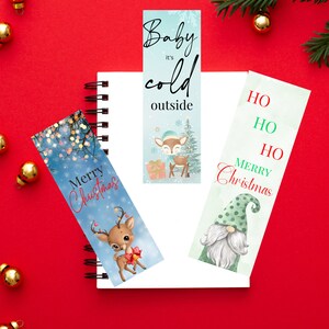 May include: Three Christmas themed bookmarks. One bookmark features a blue background with a reindeer and the text "Baby it's cold outside". Another bookmark features a green background with a gnome and the text "Ho Ho Ho Merry Christmas". The last bookmark features a blue background with a reindeer and the text "Merry Christmas".
