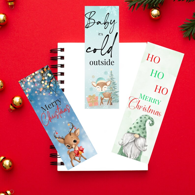 May include: Three Christmas themed bookmarks. One bookmark features a blue background with a reindeer and the text "Baby it's cold outside". Another bookmark features a green background with a gnome and the text "Ho Ho Ho Merry Christmas". The last bookmark features a blue background with a reindeer and the text "Merry Christmas".