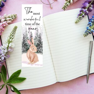 May include: A bookmark featuring a watercolor illustration of a brown rabbit sitting in a snowy forest. The text "The most wonderful time of the year" is printed at the top of the bookmark.