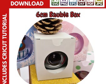 Op de afbeelding: Een witte kartonnen doos met een uitsparing om een ​​6 cm grote kerstbal te tonen. De doos is versierd met een gouden glitterrand. De afbeelding bevat de tekst "6cm Bauble Box" en "INCLUDES COMMERCIAL LICENCE".