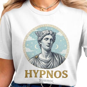 May include: White t-shirt featuring a graphic of a classical statue with winged headgear, set within a circular frame with a light blue background and crescent moons. The word "HYPNOS" is printed below the image.