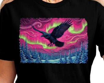 Puede incluir: Camiseta negra con un gráfico de un cuervo volando contra una aurora boreal rosa y verde. El diseño incluye un bosque de árboles azules. Un diseño llamativo con temática de la naturaleza.
