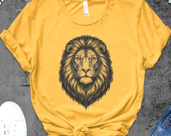 May include: Mustard yellow t-shirt featuring a detailed black and white illustration of a lion's face. The shirt is styled with a knot at the waist and is paired with white sneakers and blue jeans. A pair of white headphones is also visible.