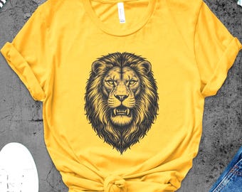 May include: A yellow t-shirt featuring a detailed black and brown illustration of a lion's head. The shirt is styled with a knot at the bottom. White sneakers, headphones, and denim jeans are also visible.
