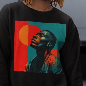 May include: Black sweatshirt featuring a colorful graphic of a person looking upwards. The graphic includes red, orange, and teal shapes. The person in the graphic is wearing a gray shirt. The person in the image is wearing a black cap.