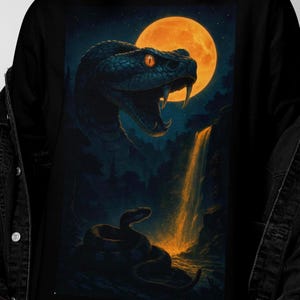 Op de afbeelding: Zwart sweatshirt met een gedetailleerde illustratie van een slang met open bek, tegen de achtergrond van een volle maan en een waterval. Het kunstwerk is uitgevoerd in donkerblauw en oranje, wat een dramatische scène creëert.