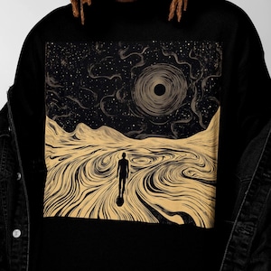 May include: Black crew neck t-shirt featuring a surreal landscape design. The artwork depicts a figure walking towards a dark celestial body in a swirling, textured environment, with a starry night sky.