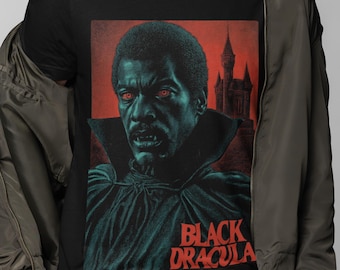 May include: Black t-shirt featuring a vintage graphic of a vampire with red eyes and a castle silhouette against a red backdrop. The text "BLACK DRACULA" is in red. The shirt is worn by a person.