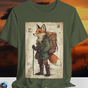 May include: Olive green t-shirt featuring a detailed illustration of a fox dressed as a hiker, complete with a backpack and walking stick. The fox is standing in front of a vintage map design. The shirt is made of a soft material.