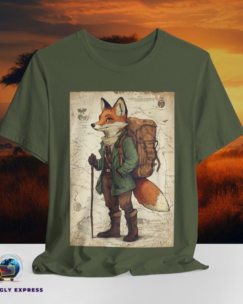 May include: Olive green t-shirt featuring a detailed illustration of a fox dressed as a hiker, complete with a backpack and walking stick. The fox is standing in front of a vintage map design. The shirt is made of a soft material.