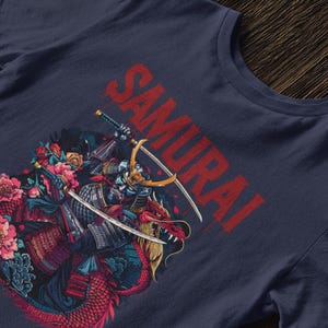 May include: Navy blue t-shirt featuring a detailed illustration of a samurai warrior riding a dragon, with the word "SAMURAI" in red. The design includes swords, flowers, and Japanese characters.