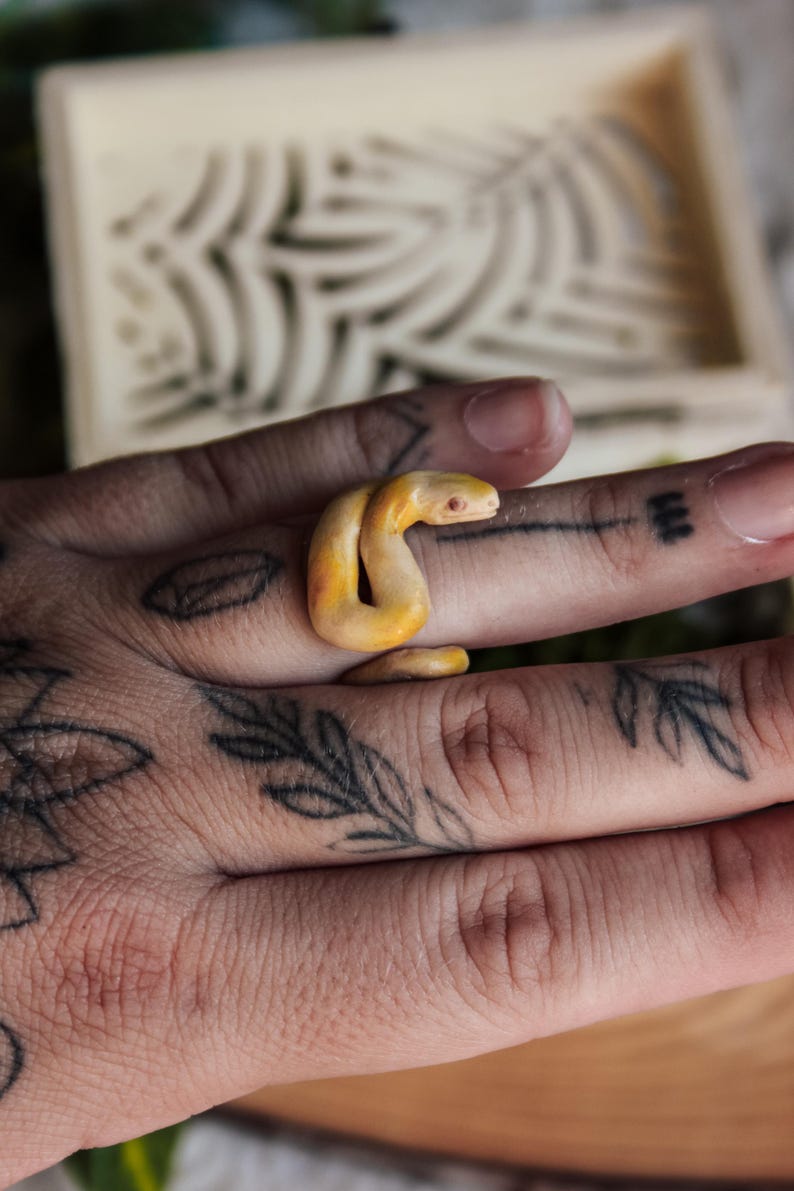 May include: A ring shaped like a coiled snake with a smooth, pale yellow and orange gradient finish. The snake features a small, distinct head with visible eye detail, wrapping around the finger in a continuous, rounded loop design.