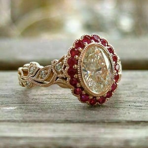 May include: Oval-shaped diamond engagement ring with a halo of red rubies. The ring band is adorned with a delicate floral design.