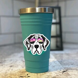 K&ouml;nnte beinhalten: Ein t&uuml;rkisfarbener Edelstahlbecher mit einem Aufkleber eines Doggen, der eine Sonnenbrille tr&auml;gt. In der Sonnenbrille spiegeln sich Palmen.