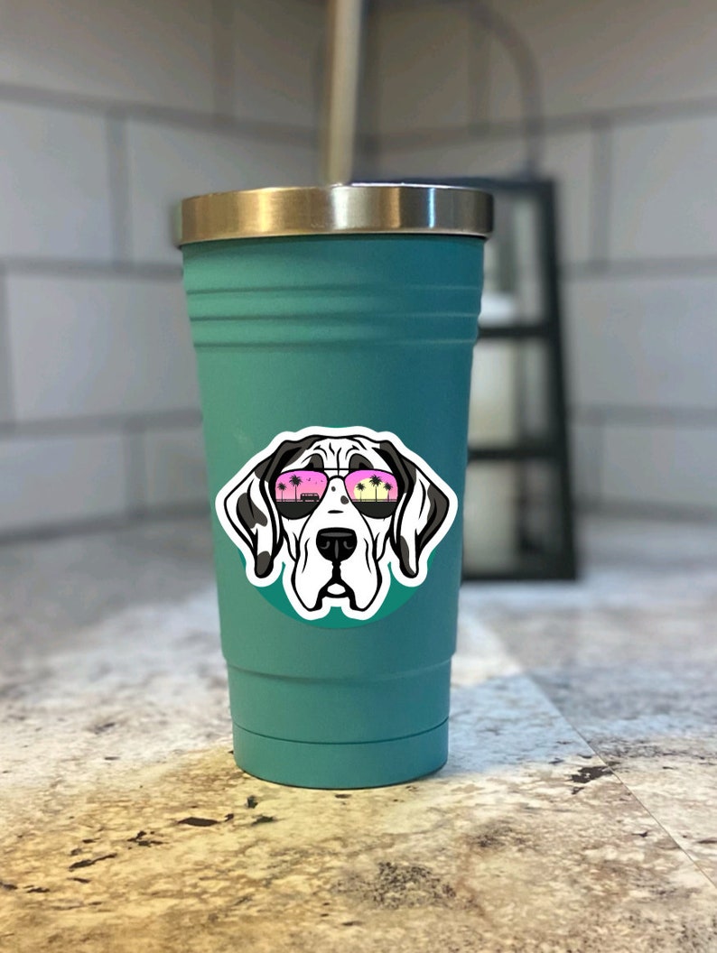 K&ouml;nnte beinhalten: Ein t&uuml;rkisfarbener Edelstahlbecher mit einem Aufkleber eines Doggen, der eine Sonnenbrille tr&auml;gt. In der Sonnenbrille spiegeln sich Palmen.