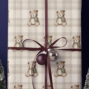 May include: A wrapped gift with a teddy bear pattern, tied with a dark red ribbon and a decorative ornament. The scene includes miniature snow-covered trees, a black car with a package on top, and a ladder, all set against a dark blue background.