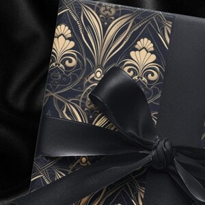 Puede incluir: Una caja de regalo negra con un dise&ntilde;o estampado en oro y negro. La caja est&aacute; atada con una cinta negra.