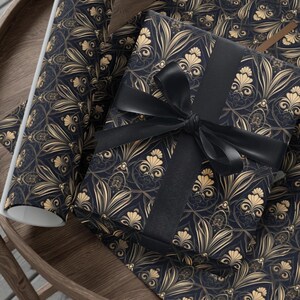 Puede incluir: Dos rollos de papel de regalo estampado en negro y dorado. Un rollo est&aacute; parcialmente desenrollado y una cinta negra est&aacute; atada alrededor.