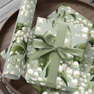May include: A green and white gift wrap with a floral pattern of white lily of the valley flowers and green leaves. A green ribbon is tied around a gift box wrapped in the same paper.