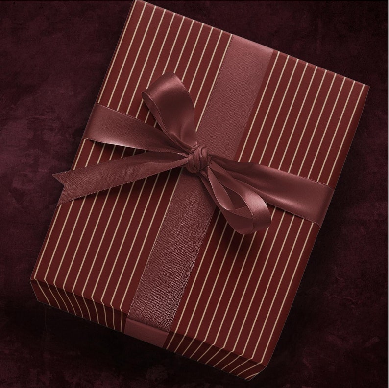 Op de afbeelding: Een bordeauxrode geschenkdoos met een gestreept patroon en een bordeauxrood satijnen lint dat in een strik is gebonden.