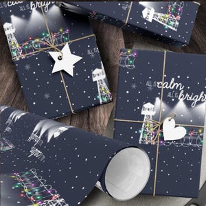 Pode incluir: Papel de embrulho azul com um design de farol branco e luzes de corda coloridas. O papel tem o texto "All is calm, All is bright" impresso nele.