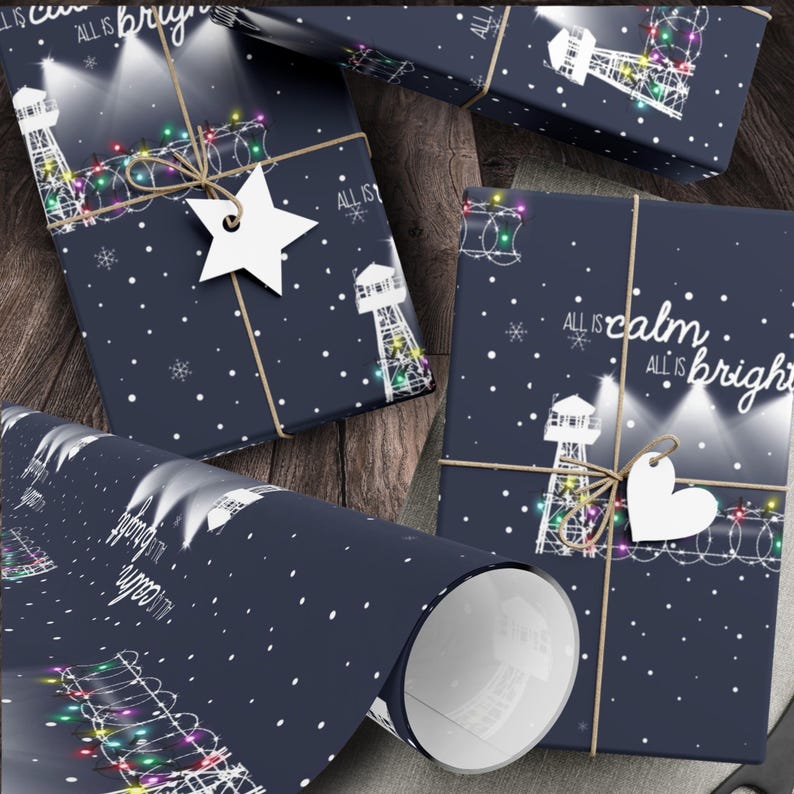 Pode incluir: Papel de embrulho azul com um design de farol branco e luzes de corda coloridas. O papel tem o texto "All is calm, All is bright" impresso nele.