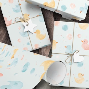 May include: Gift boxes and wrapping paper featuring a light blue background with watercolor illustrations of yellow, pink, and blue ducks, bubbles, and splashes. The boxes are tied with twine and adorned with star and heart-shaped tags.