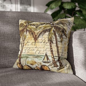 May include: Square throw pillow with a vintage beach scene. The pillow features palm trees, a sailboat, and handwritten script on a beige background. The pillow is placed on a gray sofa.