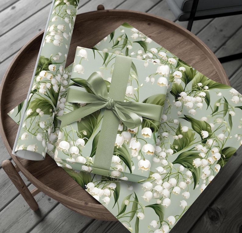 May include: A green and white gift wrap with a floral pattern of white lily of the valley flowers and green leaves. A green ribbon is tied around a gift box wrapped in the same paper.