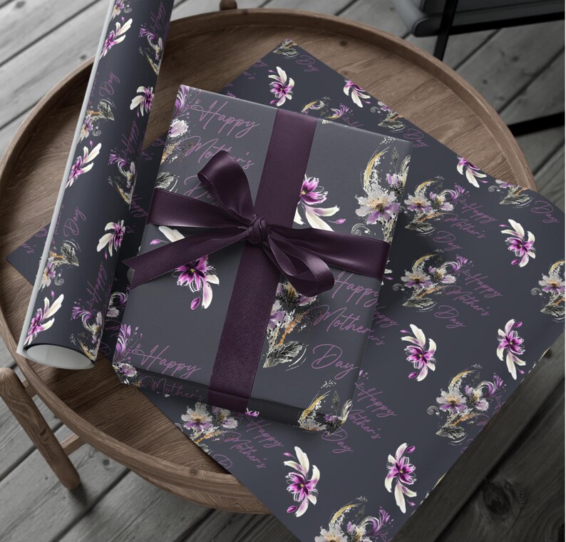 Puede incluir: Un regalo envuelto en papel de regalo azul oscuro con un patr&oacute;n floral y el texto "Happy Mother's Day". El regalo est&aacute; atado con una cinta morada.