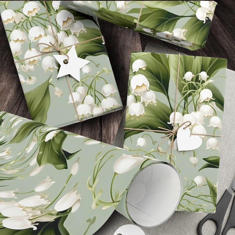 May include: Green and white floral wrapping paper with a lily of the valley pattern. The paper is rolled up and tied with twine. There is a white star and a white heart on the paper.