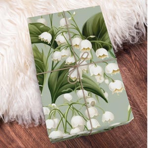 May include: A green and white floral wrapping paper with a pattern of lily of the valley flowers. The paper is tied with a brown twine bow.