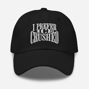 May include: Black baseball cap featuring white embroidered text: "I PREFER ICE CRUSHED". The cap has a curved peak and a button on top. The text is in a stylized font.