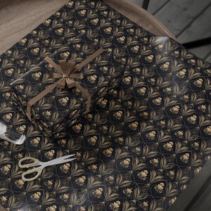Puede incluir: Papel de regalo estampado en negro y dorado con una cinta dorada atada alrededor de una caja de regalo.