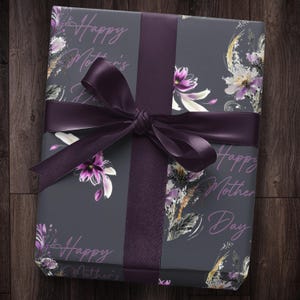 Puede incluir: Un regalo envuelto en papel de regalo gris con una cinta morada. El papel tiene un patr&oacute;n floral y el texto "Happy Mother's Day" est&aacute; impreso en &eacute;l.